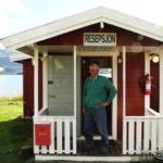 man standing in doorway to small red cabin