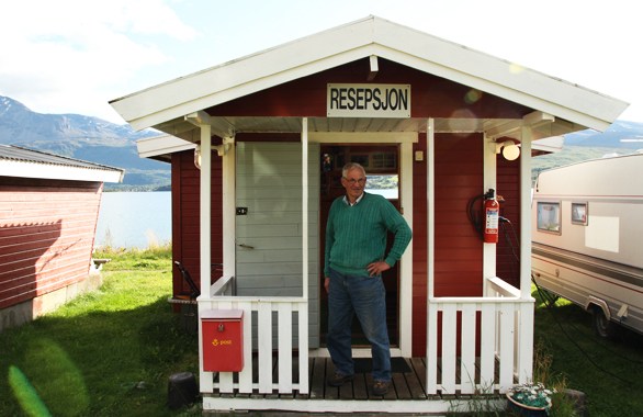 man standing in doorway to small red cabin